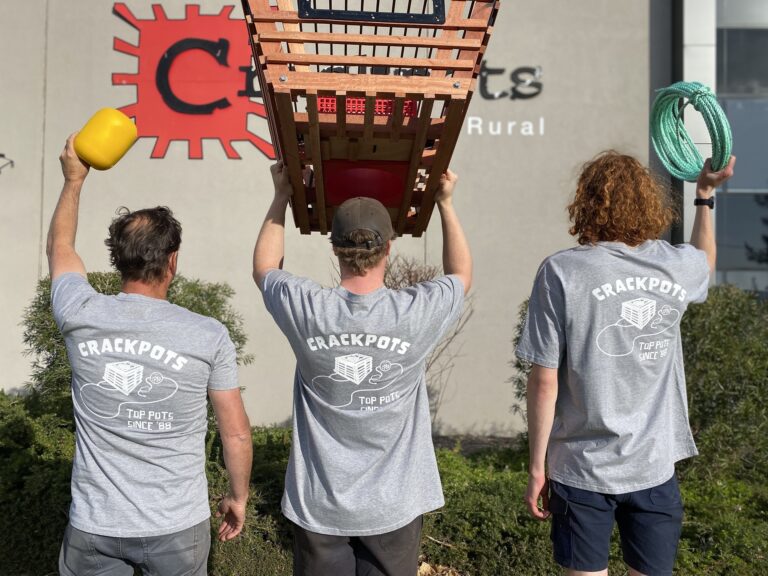 Three men in grey shirts carrying a wooden crate.